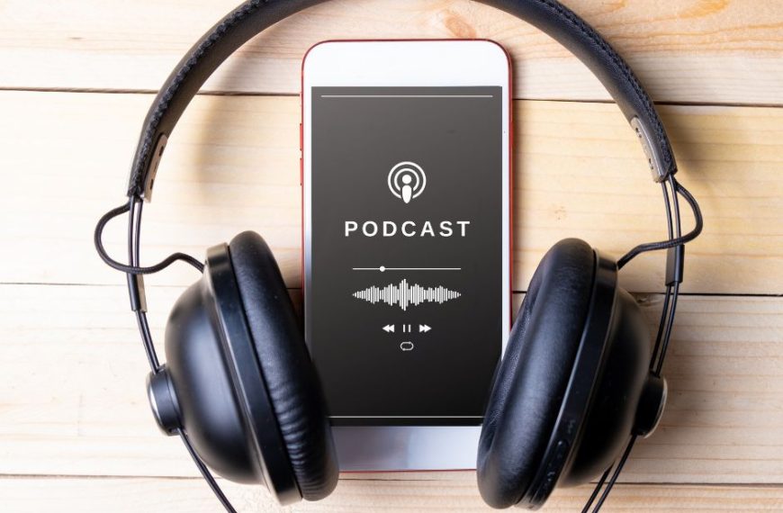 Auf dem Bild ist ein Kopfhörer und ein Smartphone zu sehen. Das Samartphone liegt in der Mitte des Kopfhörers. Auf dem Display des Smartphones steht das Wort "Podcast" Bild: Canva