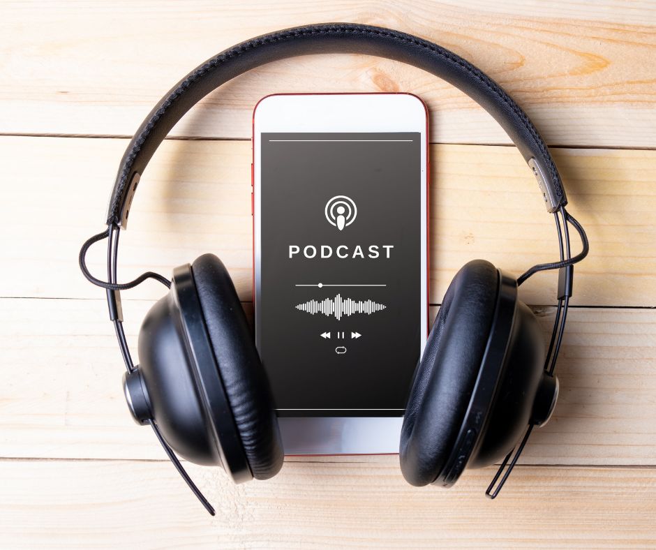 Auf dem Bild ist ein Kopfhörer und ein Smartphone zu sehen. Das Samartphone liegt in der Mitte des Kopfhörers. Auf dem Display des Smartphones steht das Wort "Podcast" Bild: Canva