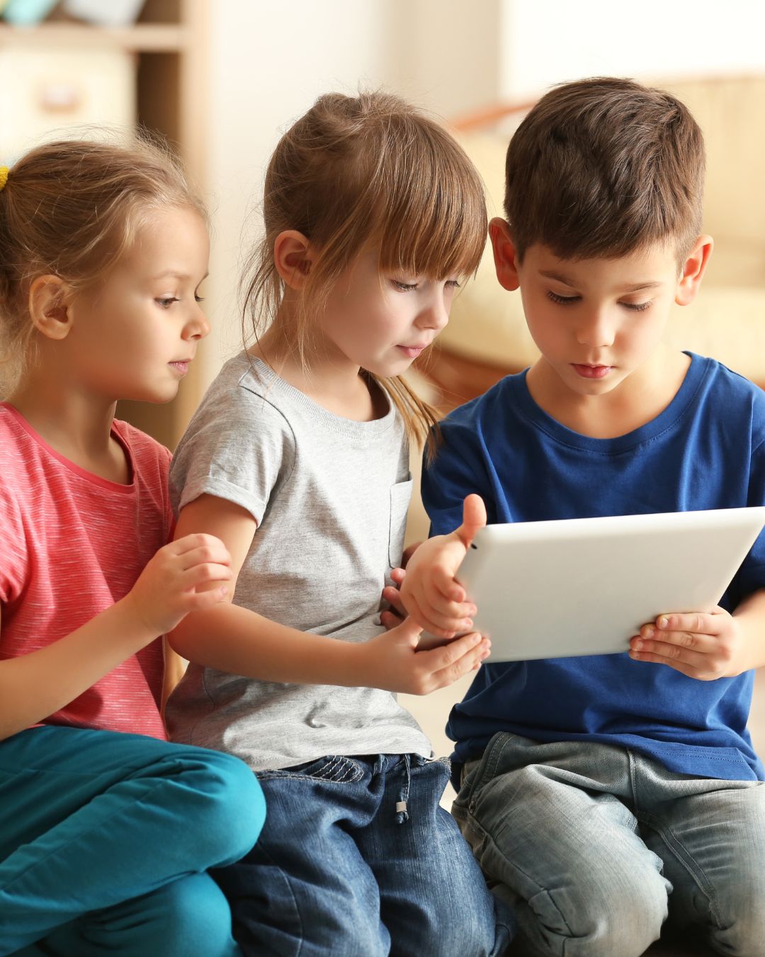 Drei Kinder, die auf ein Tablet schauen.